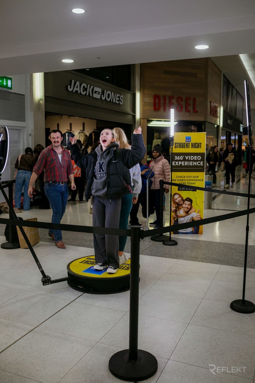 Guests on a 360 photo booth platform with stanchions at a public activation