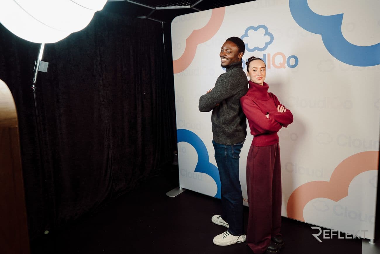 Two guests posing at a fully branded photo booth backdrop at a corporate event