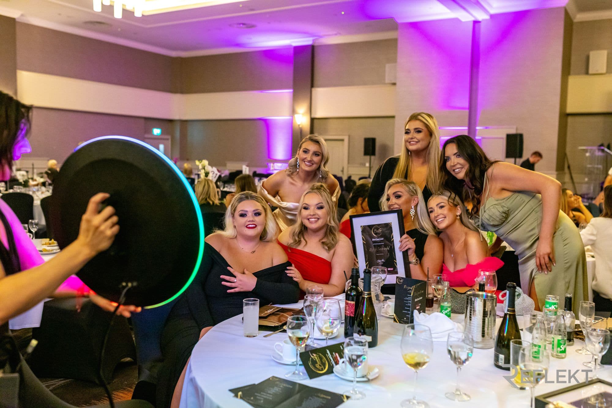 Guests at a gala table posing for a Reflekt roaming photo booth
